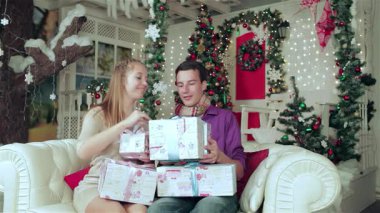 Sevecen bir çift, rahat kazaklar ve eşarplar giyip, neşeli bir şekilde paketlenmiş hediyelerini parıldayan ışıklar ve canlı bir ağaçla süslenmiş bir Noel odasında değiş tokuş ediyorlar. Bu büyüleyici sahne sıcaklığı ve sevgiyi yansıtıyor.