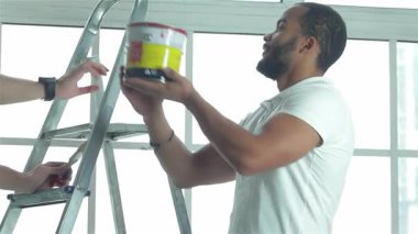 Parlak, havadar bir dairede, iki yetenekli işçi dinamik bir onarım sürecine girişirler. Bir adam, dostça bir gülümsemeyle, merdivendeki meslektaşına canlı bir kova boya uzatıyor, takım çalışması ve uzay dönüşümüne kendini adamış.