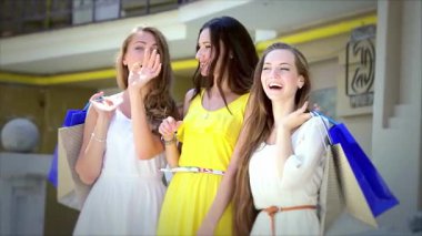 Canlı kıyafetler giymiş üç şık kız ellerinde renkli alışveriş torbalarıyla neşe ve dostluk saçarak el sallıyorlar. Kahkahaları havayı dolduruyor. Birlikte alışverişin keyifli bir gününün tadını çıkarıyorlar. Kaygısız kadınlığı somutlaştırıyorlar.