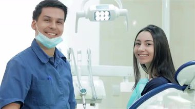 Neşeli bir dişçi ve genç bir kız hasta ışıltısı. Parlak gülüşleriyle dişçi kliniğine olan güvenlerini gösteriyorlar. Sahne, klinik atmosferi kurnazca geliştiren diş aletleri ve ekipmanlarla etkileşimlerinin sıcaklığını yakalıyor.