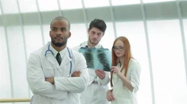 Kararlı genç bir erkek doktor kolları bağlı dururken, bir erkek ve bir kadın olan iki meslektaşı sağlıklı akciğerlerin röntgenini yakından inceliyor. Bu dinamik sahne, modern bir tıbbi ortamda takım çalışmasının özünü yakalar.