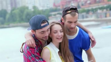 Üç neşeli arkadaş dışarıda toplanıyor, bir kızın tabletini kullanmasına yardım ederken gülüşlerini ve gülüşlerini paylaşıyorlar. Bu canlı sahne arkadaşlığın ve kaygısız yaz günlerinin özünü yakalıyor, neşe ve bağla dolu.