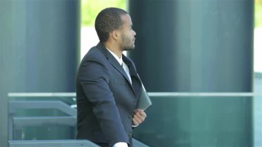 Dengeli bir Afrikalı işadamı, elinde bir tablet tutarak sıcak bir gülümsemeyle yeni ortakları karşılıyor. Modern kentsel zemin profesyonellik ve fırsat atmosferini artırarak başarılı iş dünyasının özünü gözler önüne seriyor.