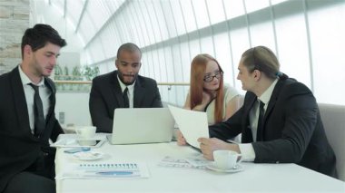 Sivri giyinmiş dört kendinden emin iş adamından oluşan bir grup, modern bir ofiste gerçekleşen bir toplantıda hayati önem taşıyan belgeleri tartışıyorlar. Gülüşleri ve jestleri, fikirleri paylaştıkça takım çalışmasının ve başarının canlı atmosferini yansıtıyor.