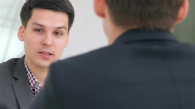 Sivri takım elbiseli genç ve çekici bir adam bir meslektaşıyla canlı bir ofis atmosferi sergileyen bir iş projesini dikkatlice tartışıyor. Sahne profesyonellik ve işbirliği içeriyor, odaklanmış ifadelerini ve modern ifadelerini vurguluyor