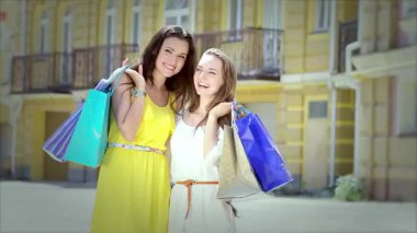 Biri canlı sarı elbiseli, diğeri şık beyaz elbiseli iki şık kız, mutluluk saçan renkli alışveriş torbaları tutuyorlar. Şakacı ifadeleri ve kaygısız tavırları arkadaşlığın özünü ve alışverişin neşesini yansıtıyor.
