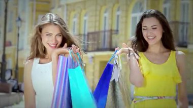 İki şık genç kadın, mutluluk saçıyor, el ele yürüyorlar, canlı alışveriş torbalarını güneşli bir arka planda sergiliyorlar. Neşeli gülümsemeleri ve kaygısız ruhları arkadaşlığın ve perakende terapinin neşesini somutlaştırıyor. Bu sahneyi mükemmel yapıyor.