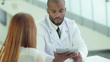 Kendini işine adamış beyaz laboratuvar önlüğü ve kravatı takmış bir doktor, tablette gösterilen bir hastanın röntgenini dikkatle inceliyor. Sahne, sağlık farkındalığının önemini ve tehlikeleri vurgulayan profesyonel bir danışma anı yakalıyor.