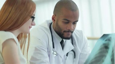 Beyaz önlüklü dost canlısı bir doktor bir hastayla temas kuruyor ve sağlıklı akciğerlerin röntgenini çekiyor. Sıcak atmosfer, sağlık ve iletişimin tıbbi bakımdaki önemini vurgulayarak bağlantılarını vurguluyor.