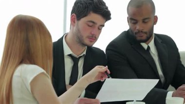 Sivri takım elbiseli üç kendine güvenen işadamı, dinamik bir toplantı sırasında önemli belgeleri incelemeye dalmış durumdalar. Atmosfer, strateji ve başarı planları tartışılırken işbirliği ve hırsla dolu.