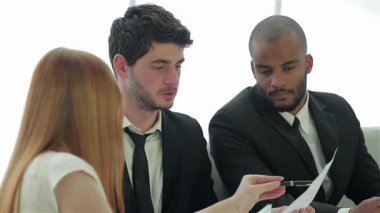 Sivri takım elbiseli üç kendine güvenen işadamı şık bir ofis masasında stratejileri tartışıyor, takım çalışması ve işbirliği sergiliyorlar. Odaklanmış ifadeleri ve jestleri yenilik ve başarının canlı atmosferini yansıtıyor.