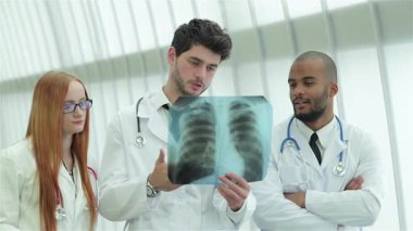 Üç kendine güvenen doktor, iki erkek ve bir kadın, sigara içmenin tehlikelerine karşı koyan sağlıklı akciğerlerin röntgenini dikkatle incelerler. Profesyonel kıyafetleri ve odaklanmış ifadeleri güçlü bir uzmanlık ortamı yaratıyor.