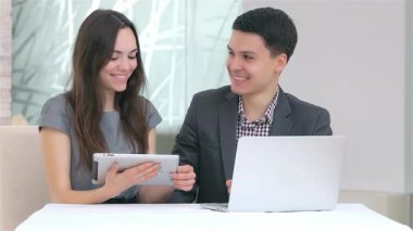 Genç, çekici bir iş adamı ve kadın şık bir tablet üzerindeki verileri analiz ederken, profesyonellik ve takım çalışması yayarak canlı bir tartışmaya girişirler. Gülüşleri ve odaklanmış ifadeleri davetkar bir atmosfer yaratıyor.