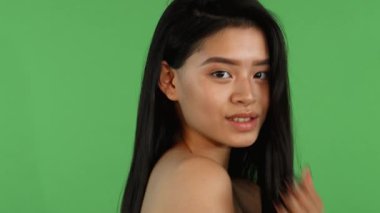 Göz kamaştırıcı genç bir Asyalı kadın canlı yeşil renkli bir arka plana karşı zarafetle poz veriyor. Parlak gülüşü sahneyi aydınlatıyor. Uzun, dalgalı saçları ve pürüzsüz cildiyle gençliğin canlılığını ve çekiciliğini somutlaştırarak izleyicileri kucaklamaya davet ediyor.