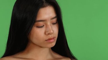 Uzun, dalgalı siyah saçları olan çarpıcı genç bir Asyalı kadın canlı yeşil renkli arka plan karşısında kameraya neşeyle ışıldıyor. Kusursuz cildi ve büyüleyici gülüşü pozitiflik ve canlılık saçıyor, özgün güzelliği somutlaştırıyor.