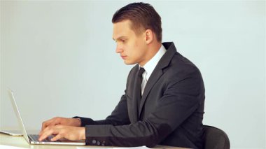 Gösterişli takım elbiseli kararlı genç bir işadamı laptopuna veri yazarak, sorunsuz bir şekilde telefona cevap veriyor. Mesleki tavrı ve odaklanmış ifadesi modern ofis ortamında birden fazla iş yapma becerisini ön plana çıkarıyor.