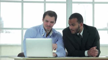 İki başarılı iş adamı, biri açık mavi gömlekli, diğeri keskin siyah takım elbiseli, düzgün bir müzakere masasında, dizüstü bilgisayardaki verileri analiz ederek odaklanmış bir tartışmaya giriyorlar. Kendine güvenen ifadeleri ve profesyonel kıyafetleri bir canlıyı yansıtıyor.