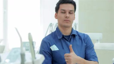 Kendine güvenen bir dişçi, parlak bir klinikte ışıldayan diş teçhizatıyla çevrili bir şekilde başparmağını kaldırırken sıcak bir gülümseme sergiler. Bu davet sahnesi, dişçilerin hasta bakımına ve oral sekse olan bağlılığını gösteren pozitiflik ve profesyonelliği yansıtıyor.