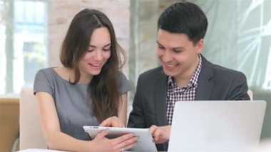 Genç, çekici bir iş kadını ve işadamı, şık bir tablet üzerinde veri toplarken, takım çalışması ve coşku yayarak canlı bir tartışmaya girişirler. Parlak gülümsemeleri ve odaklanmış ifadeleri modern bir hava yaratıyor.