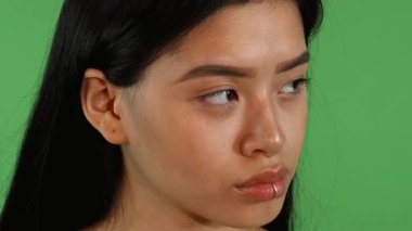 Dudaklarında piercing olan, kaşlarını kaldıran ve canlı yeşil renkli arka planına güvenle gülümseyen güzel bir Asyalı kadının büyüleyici yakın çekimi. Işıl ışıl ifadesi neşe ve canlılık yayıyor, çarpıcı özelliklerini sergiliyor.