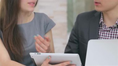 Genç, çekici bir iş kadını ve işadamının dinamik ellerini, zarif bir tablette tutkulu bir şekilde verileri tartışırken yakalıyor. Odaklanmış ifadeleri ve modern ofis arkaplanı bir işbirliği ortamı yaratıyor.