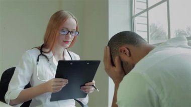 Parlak bir klinikte, şefkatli bir kadın doktor endişeli erkek hastasını dikkatle dinler. Sahne, sağlık hizmetinin özünü yakalıyor ve doktorların profesyonelliğini gösteriyor.