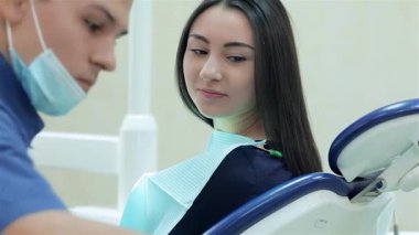 Odaklanmış bir dişçi diş aletlerini hazırlarken rahat bir hasta da rahatça sandalyeye oturup tedaviye hazır olur. Parlak klinik ortamı bakım ve profesyonellik atmosferini artırarak güven verici bir deneyim sağlar.