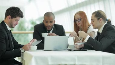 Canlı bir toplantı, dört genç profesyonel, iki erkek ve iki kadın, parlak bir ofis ortamında dumanı tüten kahve fincanları üzerine gülümseme ve fikir alışverişinde bulunurken gerçekleşiyor. Çekici sohbetleri ve işbirlikçi ruhları bir yenilik ortamı yaratıyor.