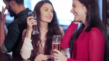 İki neşeli genç kadın, canlı bir barda kadehlerini kaldırarak arkadaşlıklarını kutluyorlar. Neşeli atmosfer kahkahalarla ve arkadaşlarıyla dolu. İçkilerinin tadını çıkarıyorlar. Arkadaşlarının tezahüratlarıyla çevrili.