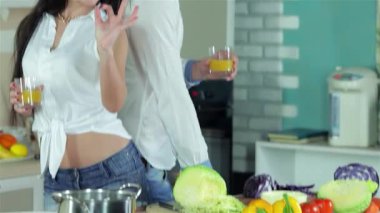 Neşeli bir çift parlak bir mutfakta sırt sırta durur, her biri elinde canlı bir bardak portakal suyu tutarken kız şakacı bir şekilde 