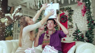 Sevgi dolu bir çift, rahat kazaklar ve eşarplar giyip, güzel süslenmiş bir Noel odasında birbirlerine güzel hediyeler veriyorlar. Peri ışıklarının sıcacık parıltısı ve çarpıcı bir Noel ağacı büyülü bir atmosfer yaratır.