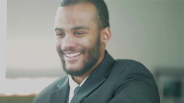 Sivri takım elbiseli, kararlı, genç bir Afrikalı işadamı, bir meslektaşıyla el sıkışıyor, profesyonelliği ve başarıyı somutlaştırıyor. Parlak ofis ortamı işbirliği ve başarı atmosferini geliştirir, dinamiği gösterir