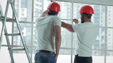 Parlak, havadar bir dairede, iki yetenekli işçi titizlikle pencereleri ölçüyor ve onarımlara hazırlanıyor. Odaklanmış ifadeleri ve takım çalışmaları, yakınlarda bir merdiven ve vaatlerle bu alanı dönüştürmeye olan bağlılıklarını vurguluyor.