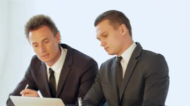 Birinde dikenli saçlı, diğerinde parlak görünümlü iki keskin giyimli işadamı, modern bir masada profesyonelliklerini ve takım çalışmalarını sergileyerek bir iş planını dikkatle tartışıyorlar. Analizler sırasında atmosfer hırsla doludur.