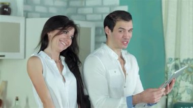 Neşeli bir çift sıcak bir mutfakta durup tablet üzerinde canlı sebze güveci tarifleri keşfediyor. Taze malzemeler ve renkli sebzelerle çevrelenmiş olarak birlikte lezzetli bir yemek hazırlarken kahkahaları havayı dolduruyor.