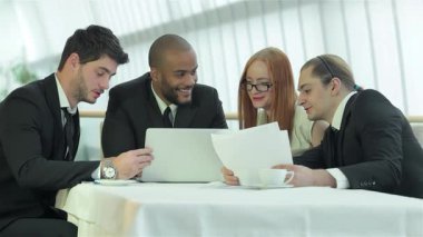 Kendine güvenen dört profesyonel, parlak bir ofis ortamında dizüstü bilgisayar ve belgeler üzerinde fikir alışverişinde bulunarak canlı bir tartışmaya girişiyor. Gülüşleri ve odaklanmış ifadeleri başarılı bir takım çalışması atmosferini yansıtıyor ve işbirliğinin özünü vurguluyor.
