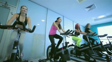 Dört enerjik arkadaş spor salonundaki sabit bisikletler üzerinde hareketli bir fitness seansına katılıyor, kararlılıklarını ve arkadaşlıklarını sergiliyorlar. Renkli spor kıyafetleriyle canlı atmosfer güçlenir. Takım çalışmalarını ve güçlerini vurgularlar.