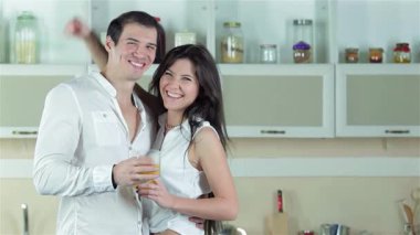 Neşeli bir çift, canlı sebzelerle çevrili mutfak masalarında kameraya parlak bir şekilde gülümsüyor. Baş parmağı havada ve elinde bir bardakla, birlikte yemek pişirmenin hazzını somutlaştırıyorlar, sevgi dolu ve hoş bir atmosfer yaratıyorlar.