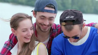 Üç neşeli arkadaş, bir kadın ve iki erkek, suyun kenarında selfie çekerken kahkahalarla gülüyorlar, neşe ve dostluk saçıyorlar. Bu canlı sahne, güneşli bir günde arkadaşlığın özünü yakalar. Gülücükler ve kaygısız anlarla dolu.