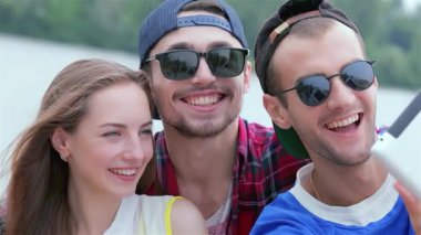 Üç neşeli arkadaş, bir genç kadın ve iki erkek, neşeyle suyun kenarında selfie çekiyorlar, mutluluk ve dostluk yayıyorlar. Parlak gülümsemeleri ve şık güneş gözlükleri kaygısız bir yaz atmosferini yansıtıyor. Bu anı mükemmel bir enstantane haline getiriyor.