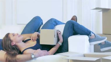Sevinçli bir çift, yeni evlerindeki paketsiz kutularla çevrili, rahat beyaz bir kanepede uzanır. Gülüşleri mutluluk saçıyor birlikte parlak bir gelecek düşlerken, yeni başlangıçların heyecanını somutlaştırıyor.