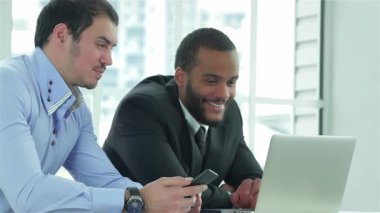 Birinde akıllı telefon, diğerinde dizüstü bilgisayara odaklanmış iki kendine güvenen işadamı şık bir ofis masasında canlı bir tartışmaya girişiyor. Resmi kıyafetleri ve coşkulu ifadeleri verimli bir atmosferi, takım çalışmasını ve
