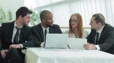 Sivri iş kıyafetleri içinde dört kendinden emin genç profesyonelden oluşan bir grup, parlak ofis ortamında aromatik kahve konusunda fikir alışverişinde bulunuyor. Gülüşleri ve hareketleriyle, canlı bir işbirliği ve başarı atmosferini yansıtıyorlar.