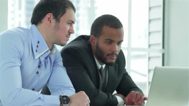 Gösterişli, çağdaş bir ofiste, iki genç iş adamı bir dizüstü bilgisayar üzerinde çalışırken odaklanmış bir tartışmaya girişiyor. Keskin resmi giysiler içindeki ifadeleri, başarı için strateji kurarken azim ve dostluğu yansıtıyor.