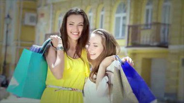 İki şık kız, biri parlak sarı elbiseli, diğeri de sıradan bluzlu, ellerinde renkli alışveriş torbalarıyla sıcacık sarılıyorlar. Işıl ışıl gülüşleri ve kaygısız kahkahaları arkadaşlığın ve eğlencenin özünü yansıtan canlı bir atmosfer yaratıyor.