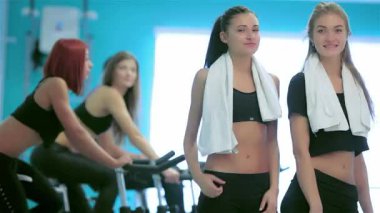 Canlı bir spor salonu ortamında, iki fit arkadaş kameraya gülümserken, arkadaşları hareketsiz bisikletlerle pedal çevirirken başparmaklarını kaldırıyorlar. Bu canlı sahne, dostluğun özünü yakalıyor ve fitness 'e olan bağlılığını gösteriyor.