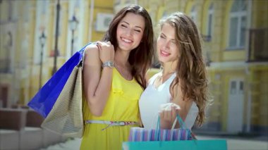 İki şık kız, canlı alışveriş torbalarıyla güneşli caddede güneşlenirken mutluluk saçıyor. Gülüşleri ve kaygısız ruhları arkadaşlığın özünü ve başarılı bir alışveriş çılgınlığının heyecanını yakalar.