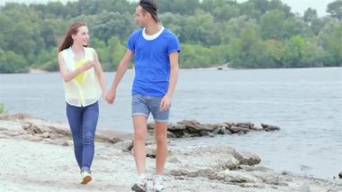 Neşeli genç bir çift, berrak bir gökyüzü altında gülücükler ve kahkahalar atarak sakin kıyı şeridinde geziniyor. Sevgi ve dostlukla dolu mükemmel bir yaz gününü yakalayan neşeli bağları sıcaklık saçıyor.