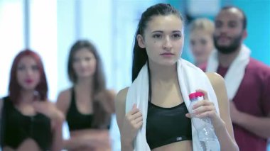 Kendine güvenen genç bir sporcunun çarpıcı portresi, elinde su şişesi olan ve destekleyici arkadaşlarıyla dolu canlı bir spor salonunda. Bu enerjik sahne, takım çalışmasının ve kararlılığın özünü yakalar.