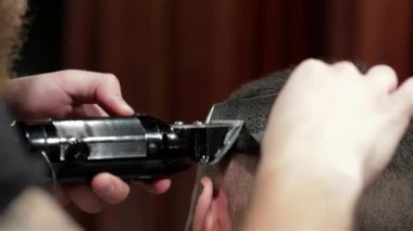 Şık bir berber dükkanında, yetenekli bir berber titizlikle sakallı bir adamın saçlarını kesiyor, hassasiyet ve sanat eserleri sergiliyor. Kaliteli dekor ile vurgulanan sıcak ortam, tımar ve stil için hoş bir ortam yaratıyor.